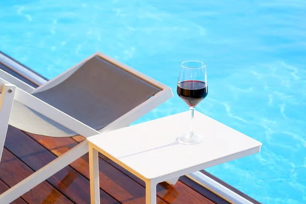 プールの反対側の夏椅子のそばのテーブルに赤ワインのガラス 残りのコンセプトです ホテルの部屋のテラスにプールのフラグメント — ストック写真