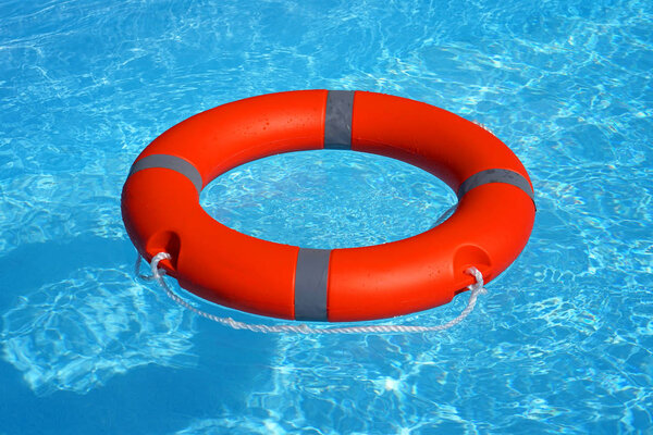 Red lifebuoy pool ring float on blue water. Life ring floating on top of sunny blue water. Life ring in swimming pool