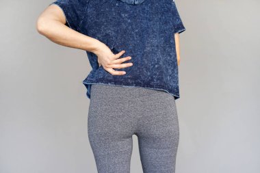 Gri bir arka plan üzerinde izole böbrek ağrısı olan bir genç kadın görmek. Genç kadın elini Sırtının alt clasping sırt ağrısı ile. Lastik ağrısı, bel ağrısı acı kadın.