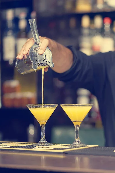 Barmen el Turuncu bir kokteyl cam içine dökülen. Barmen pişmiş malzemeler bir soğutulmuş kokteyl barda içine dökülen. Yakın çekim.
