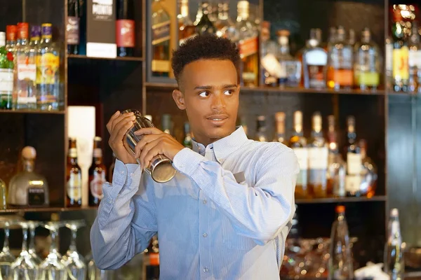 Professional bartender man holding in hands a shaker with a fresh delicious cocktail. Bartender shaking a cocktail shaker as she stands behind the bar mixing a drink for a client. Close-up.