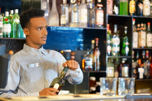 The barman is holding a bottle of whiskey. The barman examines a bottle of whiskey. The bartender pours whiskey to the client in the hotel bar. The concept of service. Concentrate on the bartender.