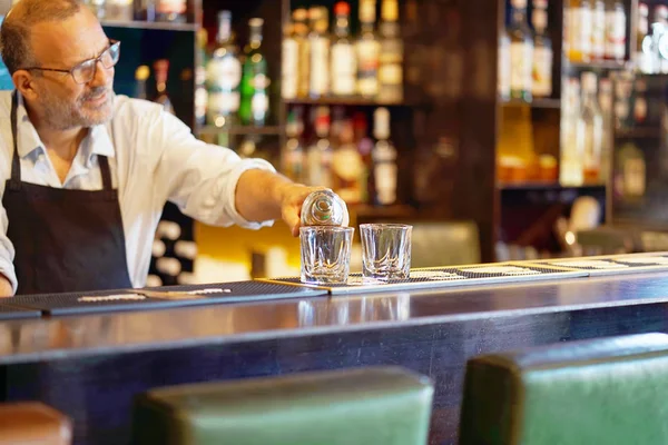 Bartender man pours whiskey to the client of the hotel bar. The concept of service. Focus on the glass.