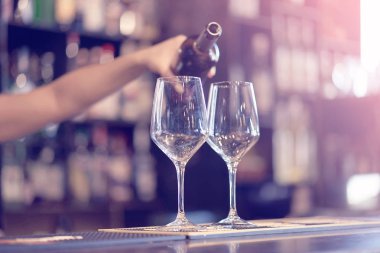 El bir barmen kız beyaz şarap bir şişe cam içine dökülen. Raflar şişe alkol arka plan ile. Cam üzerine odaklanır. Tonlama