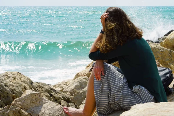 Üzgün yalnız kız deniz yakınındaki kayaların üzerinde oturuyor. Depresyon kadın hisseder.