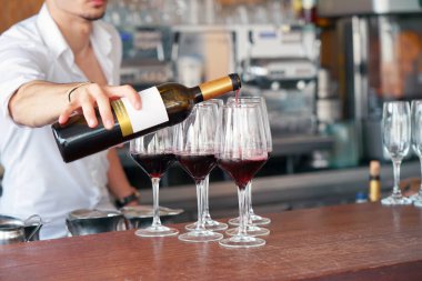 Ayakta, bir barmen erkekler kırmızı şarap bir şişe cam içine dökülen. Raflar şişe alkol arka plan ile. Cam üzerinde odaklanmak.