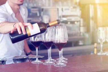 Ayakta, bir barmen erkekler kırmızı şarap bir şişe cam içine dökülen. Raflar şişe alkol arka plan ile. Cam üzerine odaklanır. Tonlama