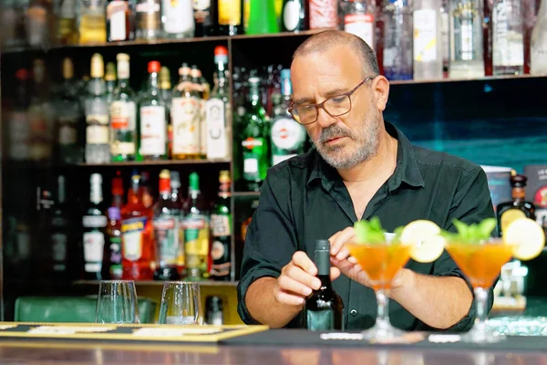 A bartender men smiles and opens a bottle of white wine for the client of the hotel bar. Shelves with bottles of alcohol in the background. The concept of service.