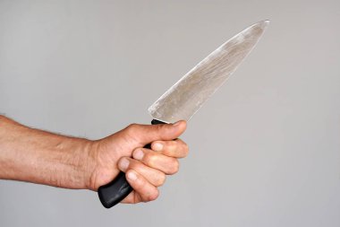 Elinde bir bıçakla gri bir arka plan üzerinde izole bir adamın elini. Adam elinde büyük bir mutfak bıçak.