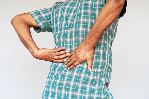 Close-up view of a young african man with pain in kidneys on gray background. Young man with back ache clasping her hand to her lower back. Man suffering from ribbing pain, waist pain.