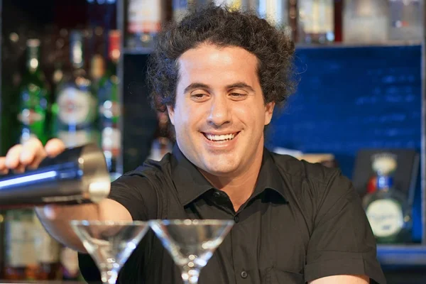 Professional barman man pours a fresh cocktail to the customers of the hotel bar. Focus on the bartender. The concept of service.