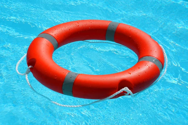 红色救生圈漂浮在蓝色的水面上 生活环漂浮在阳光灿烂的蓝色水面上 游泳池里的救生圈 — 图库照片