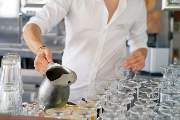 The barman pours a drink into the glass. bartender pouring juice from a pitcher iron. The concept of service.