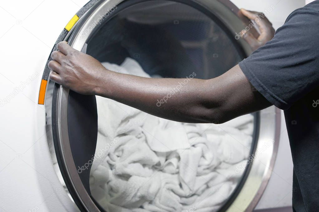 The hands of an african male laundry worker in the inn give a clean towel from the washing machine. Washing machine in stylish hotel laundry. Laundry in the hotel.