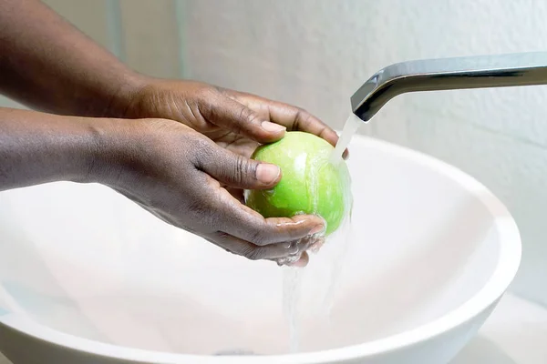 Female hands wash the green apple under the tap. Woman young housewife washing fresh green apple in kitchen under water stream. Healthy eating.