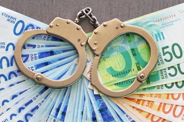 İsrail para arka plan üzerinde kelepçe. 50, 100 ve 200 Yeni İsrail para faturaları (banknot) şekel. Polis kelepçe. Mali suç, kirli para ve yolsuzluk kavramı.