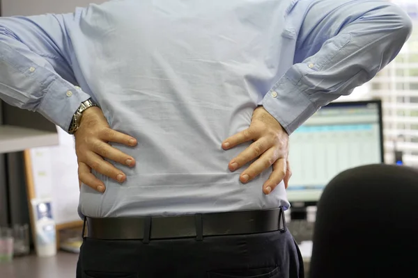Close-up view of a office worker man with pain in kidneys. Young male with back ache clasping her hand to her lower back. Men suffering from ribbing pain, waist pain.