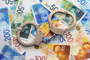 İsrail para arka plan üzerinde kelepçe. 50, 100 ve 200 Yeni İsrail para faturaları (banknot) şekel. Polis kelepçe. Mali suç, kirli para ve yolsuzluk kavramı.