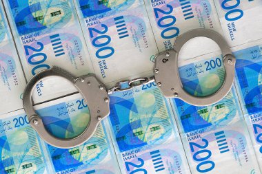 İsrail para arka plan üzerinde kelepçe. Yeni İsrail para reçeteleri (banknot) 200 şekel. Polis kelepçe. Mali suç, kirli para ve yolsuzluk kavramı.
