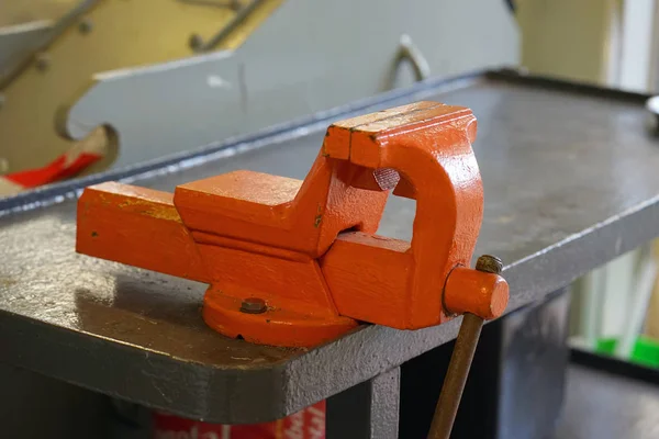 Close-up orange clamp mounted grip with screw action grip and cast iron frame, in a machining workshop. Large Iron Vise on the Desktop in a farm.