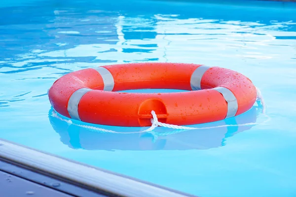 红色救生圈漂浮在蓝色的水面上 生活环漂浮在阳光灿烂的蓝色水面上 游泳池里的救生圈 — 图库照片