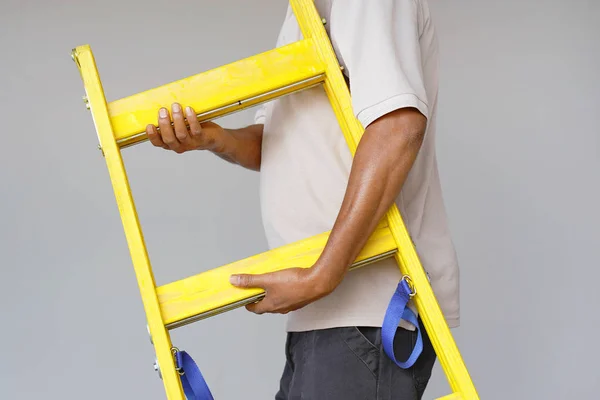 电工持有黄色木梯 建筑工人在灰色背景上有一个木阶梯 工厂工人用黄色木楼梯 — 图库照片