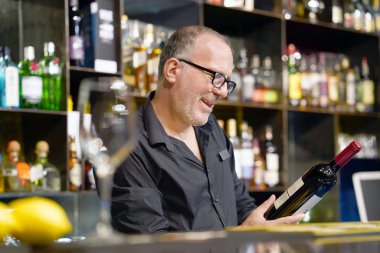 Barmen bir şişe kırmızı şarap tutuyor. Barmen bir şişe kırmızı şarap inceliyor. Barmen istemciye kırmızı şarap otelin barında içki alıyor. Hizmet kavramı. Barmen üzerinde konsantre.