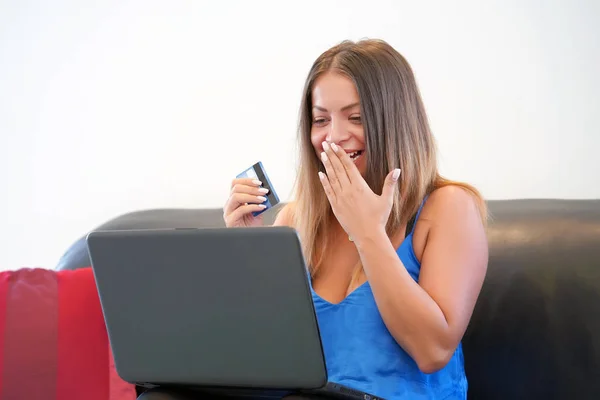 Woman with a credit card at home. A young girl buys online. A woman is holding a credit card and is using a laptop. The concept of online shopping. Close-up.