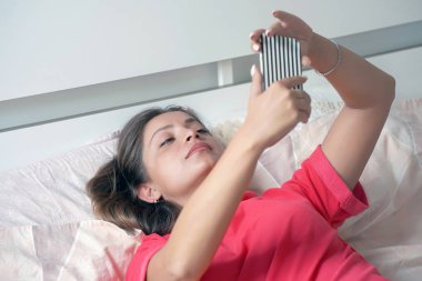 Woman using a mobile phone lying on the bed at home. Sexy beautiful woman with a smartphone in bed. Young woman using smartphoneon enjoying social networks in bed. clipart