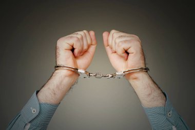Yakın çekim. Tutuklanan adam gri arka plan üzerinde izole elleri kelepçeli. Mahkum veya tutuklanan terörist, elleri kelepçeli yakın çekim.