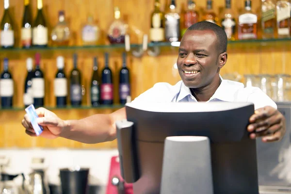The barman gives the card to the client. Registration male of bartender employee of a new order by a cash register. The barman pays the order with a credit card. Service concept.