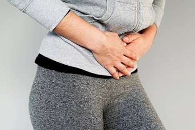 Gri arka plan üzerinde izole acı karın ağrısı olan genç bir kadın görmek. Kronik gastrit. Beden ve sağlık kavramı.