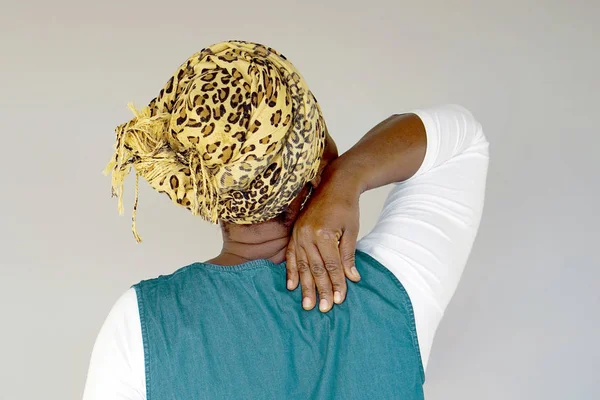 African elderly woman in scarf with pain in her back isolated on a gray background