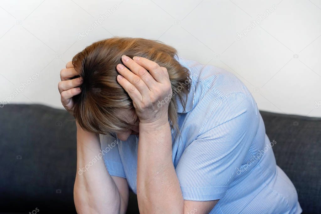 Loss of a loved one. Sadly depressed elderly woman at home, sitting on the couch. A very unhappy woman mourns the loss of her husband. Very sad woman. Concept of loneliness and pain of the penioners.