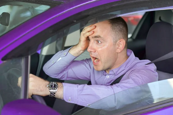 Side window view of inexperienced anxious motorist. Man driving a violet car shocked about to have traffic accident, windshield view. Scared funny looking young man driver in the car.