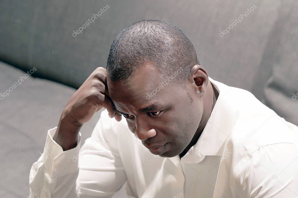 Lonely african man is sad sitting on the bed. Portrait of a sad male close-up. Man feel depression.