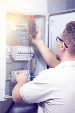 Elektrikçi erkek ile elektrik kabine multimetre gerilim ölçer. Elektrikçi elektrik kutusunda bir voltaj kontrol ediyor. Tonlama