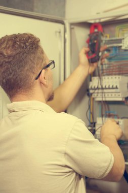 Elektrikçi erkek ile elektrik kabine multimetre gerilim ölçer. Elektrikçi elektrik kutusunda bir voltaj kontrol ediyor. Tonlama