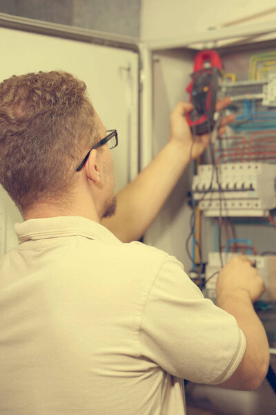 Electrician male measures voltage with multimeter in electrical cabinet. An electrician is checking the voltage in an electric box. Toning