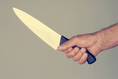 Elinde bir bıçakla gri bir arka plan üzerinde izole bir erkek eli. Yakın çekim büyük bir mutfak bıçağı adamın elinde. Tonlama