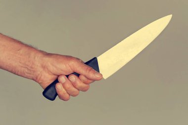 Elinde bir bıçakla gri bir arka plan üzerinde izole bir erkek eli. Yakın çekim büyük bir mutfak bıçağı adamın elinde. Tonlama