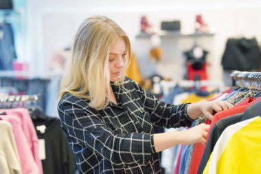 Genç sarışın kız, depodaki yeni şeyler seçin. Güzel genç kadın müşteri seçer butik bir şeyler sevdim. Genç bir kız bir askı şeylerde bir mağazada seçer. İkinci el dükkanı.