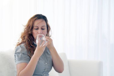 Depresif sağlıksız Kızıl saçlı kadın, ağrılı dönemler için antidepresan hapı, acil durum gebelik önleyici, ağrı kesici hakkında almak. Hap bardak su evde kanepede tutan hasta kadın.