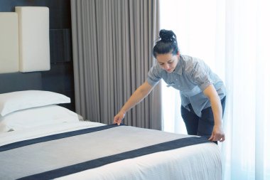 Maid making bed in hotel room. Housekeeper Making Bed clipart