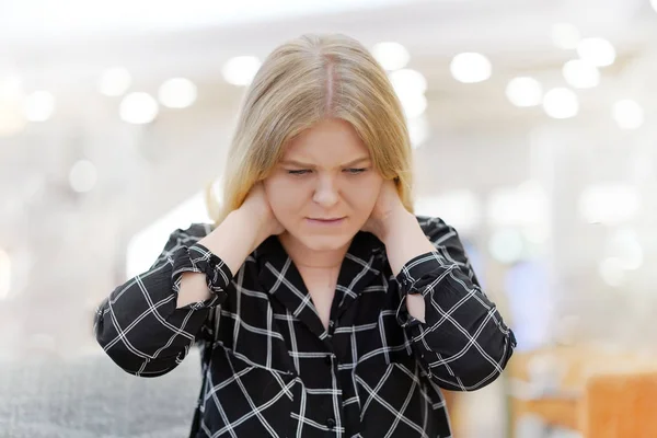 Young girl suffering from neck pain at cafe on couch. A woman\'s sense of fatigue, exhausted, stressed. A girl massages her painful neck with her hands. The concept of body and health.