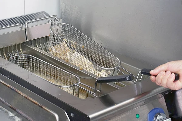 The cook fries fish in a deep fryer. Preparation in a deep fryer. Deep fryer with boiling oil on restaurant hotel kitchen