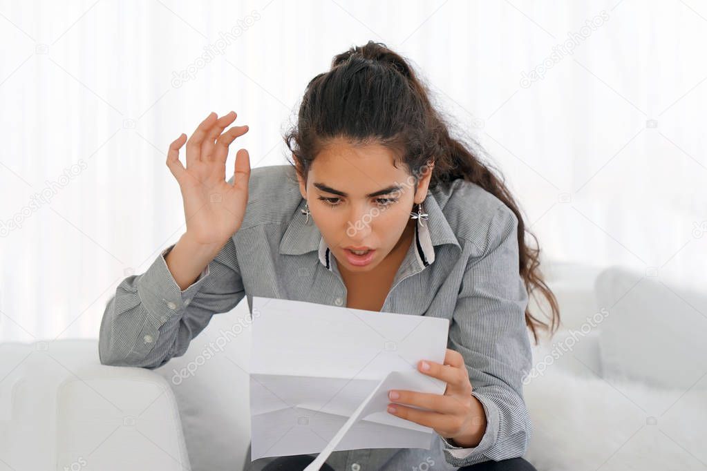 Young woman reads negative news in a letter at home on the couch. The shaken business manager of the beauty girl received a notice of dismissal from the company, surprised. An agitated girl without joy.