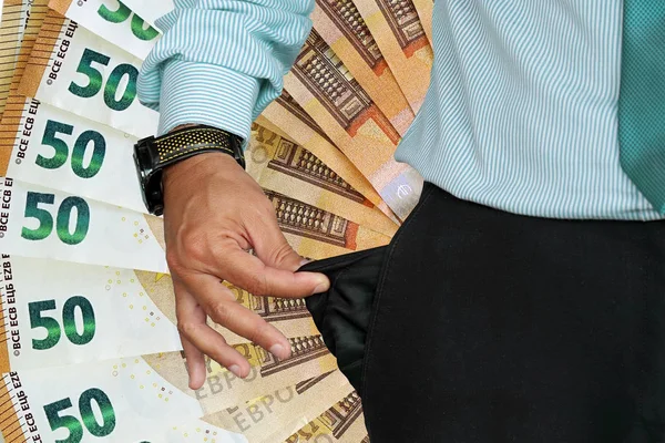 Close-up of hand of senior businessman in suit turning pocket of his trousers inside out and showing it empty. Crisis, unemployment, bankruptcy concept. Fan of 50 euro in the background.