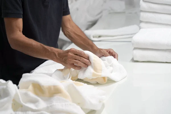 Hands of caucasian male laundry hotel worker folds a clean white towel. Hotel staff workers. Hotel linen cleaning services.