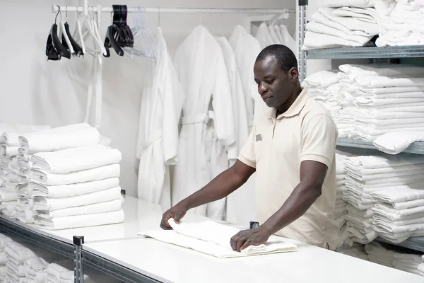 An African male hotel worker folds a clean white towel. Hotel staff workers. Hotel linen cleaning services.